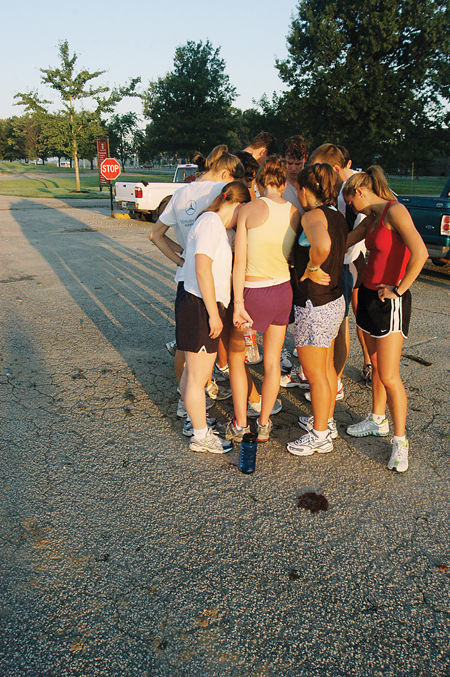 The cross country teams gather together for a quick prayer in the parking lot as the sun rises following the teams second early-moring practice of the season. - Photo by Brad Moore