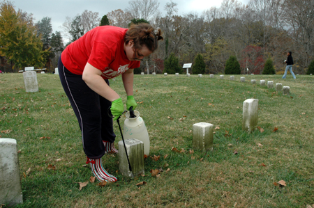 Phi Alpha Theta member Cassie Harris cleans gravestones in the national cemetery at Fort Donelson on Day of Remembrance. - Photo by Jim Veneman