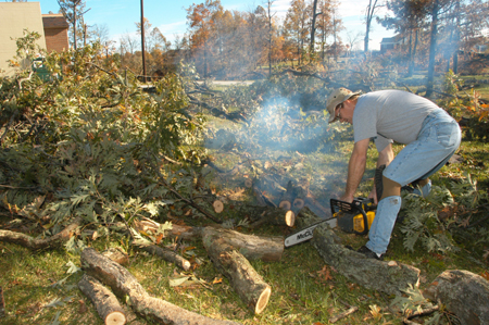 Christian Studies professor Paul Jackson uses a chainsaw to help clear trees downed by the tornado behind the McAfee Residence Complex. - Photo by Jim Veneman