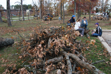 After a long day of hauling tornado-downed tree limbs, a few students take a break to re-live some moments from the past 39 hours. Pictured in front of the grove behind the McAfee Residence Complex from right to left: James Lux, a junior from Memphis; Rebecca Phillips, a junior from Chattanooga; Carrie Thomas, a senior from Nashville; and Bamby Cho, a junior from Belize City, BH. - Photo by Jim Veneman