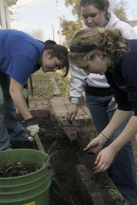 Megan Ditter, Miranda Lindsey and Emily Babin work on a garden bed at The Care Center during Day of Remembrance. The girls weeded out the bed and secured a brick lining around the edge of it. - Photo by Kyle Kurlick