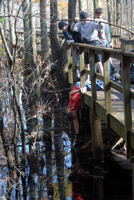 Nathan Cobb reaches for trash under the boardwalk at Cypress Grove Nature Park. Cypress Grove was visited by twenty students, staff and faculty from Union University on the Day of Remembrance. - Photo by Morris Abernathy