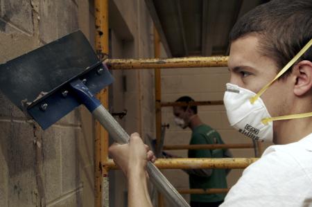 Casey Kidd and Luke Burleson work on a gym wall at the Augustine school scraping paint off to prepare for a fresh coat during Day of Remembrance. - Photo by Kyle Kurlick