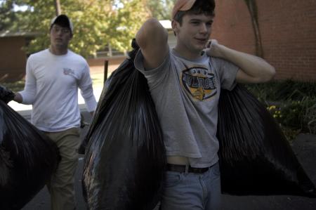 Scott Riessen, right, and Tyler Merriam, left, carry leaf-filled garbage bags to the dumpster at the Augustine School where they and fellow SAE members are spending Day of Remembrance cleaning the grounds of the school. - Photo by Kyle Kurlick