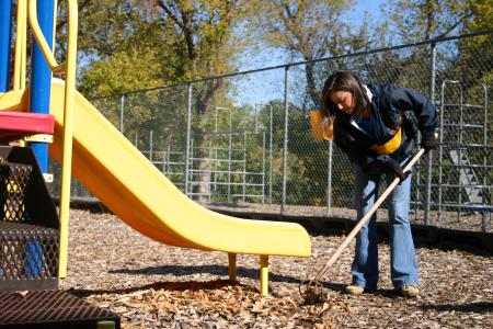Freshman Cherish Cooper rakes wood chips to cover mud holes on a playground set at Whitehall Elementary School during Day of Remembrance. - Photo by Stephanie Schroeder