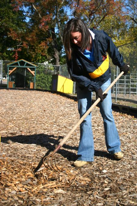 Freshman Cherish Cooper rakes wood chips to cover mud holes on a playground set at Whitehall Elementary School during Day of Remembrance. - Photo by Stephanie Schroeder