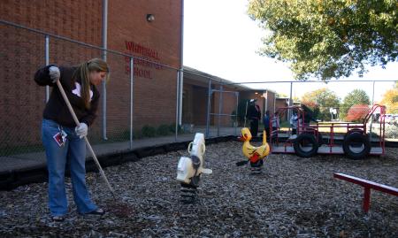 Freshman Elizabeth Wainscott rakes wood chips to cover mud holes on a playground set at Whitehall Elementary School during Day of Remembrance. - Photo by Stephanie Schroeder