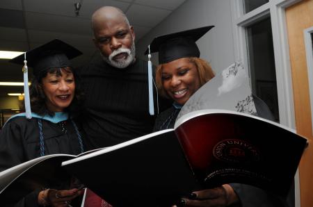 Marilyn Locke, left, and her fiancé Pierre Nelson both of Memphis, along with Portia Brown, also from Memphis, look over the graduation program moments before service begins. Locke and Brown received the Masters of Arts in Education degree during the summer graduation at Union University. - Photo by Jim Veneman