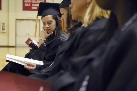 Madolyn Maupin (far left), looks over at her neighbor's program during the graduation ceremony in the Fred DeLay Gymnasium. Maupin is graduating with a Bachelor of Science in Nursing. - Photo by Justin Veneman