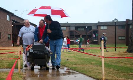 Larry Vaughan, assistant director of church relations (center); and Jerry Tidwell, senior VP for church relations (right); carefully shelter Joe Caldwell's (left) student's television from the rain, while still maintaining conversation, on new student move-in day. - Photo by Kristi McMurry Woody