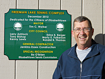 Bo O'Brien smiles next to the Freeman Lake Tennis Complex sign.