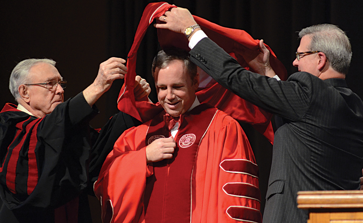Hyran Barefoot and Norman Hill aid in the hooding process during Dub Oliver's presidential inauguration.