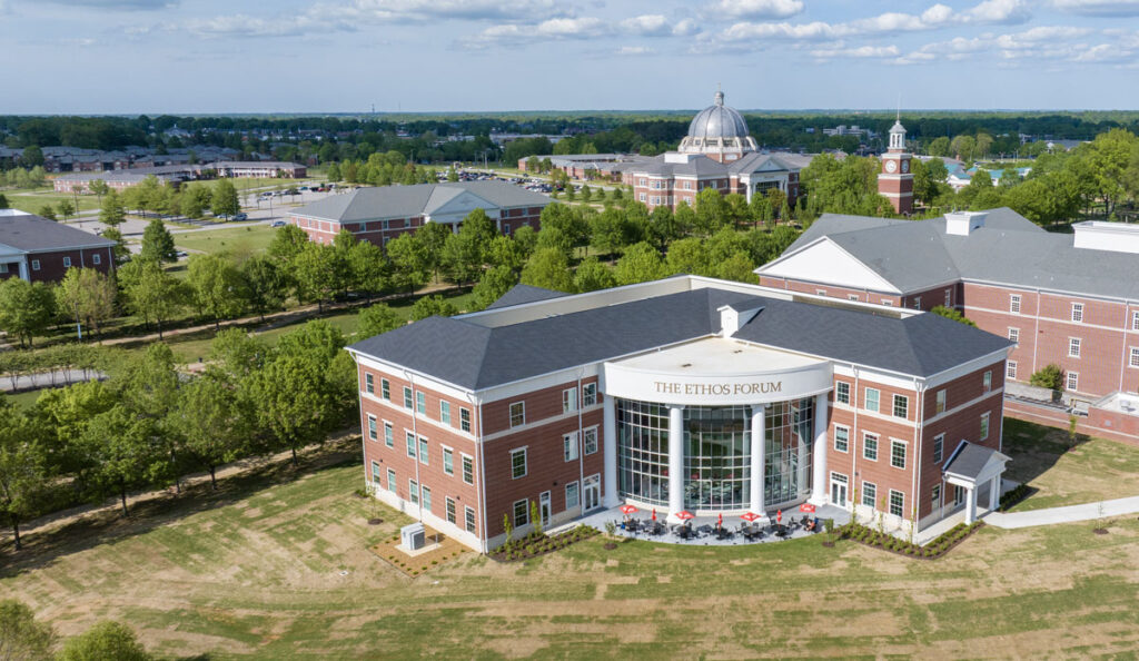 Aerial view of the modern brick academic building, The Ethos Forum, on Union's campus—its recent dedication celebrated amid lawns, trees, outdoor seating, and neighboring buildings under a blue sky with scattered clouds.