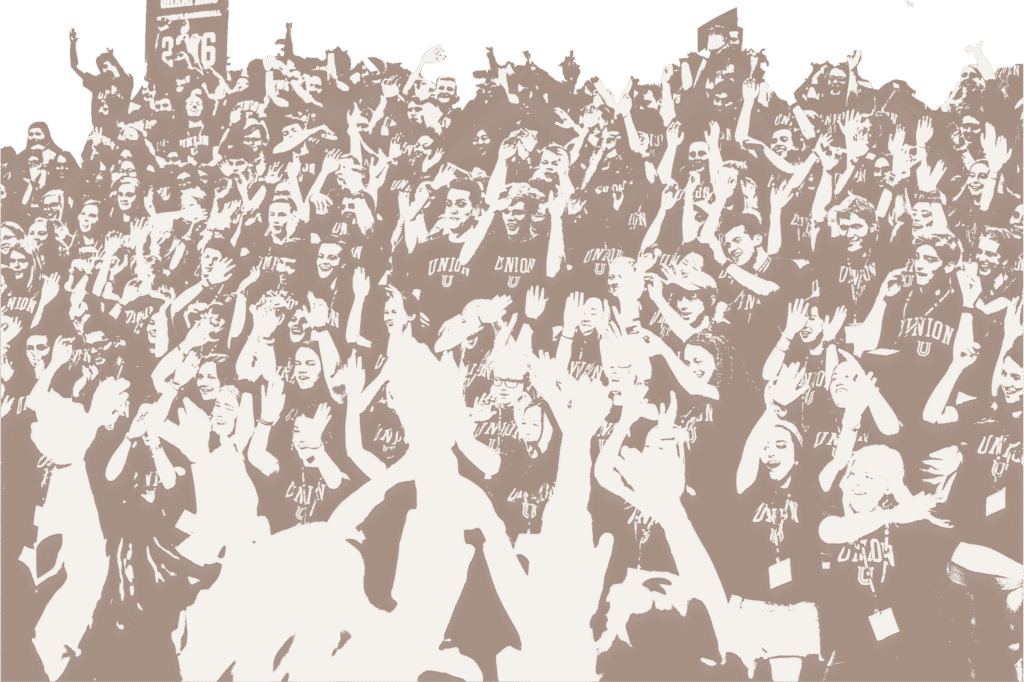 A large group of people wearing matching shirts stands together, many with arms raised and hands waving, creating an energetic and celebratory atmosphere.