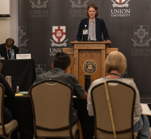 A woman stands at a podium speaking to an audience at Union University in Jackson. A panelist sits at a table to her left, and several people are seated facing her. The university’s logo and name appear on the backdrop.