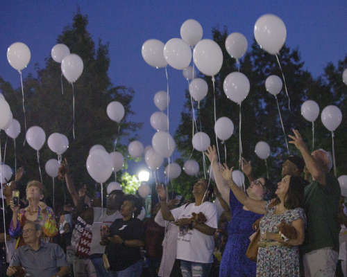 At dusk on Sept. 29, homicide loss survivors gather for the Remember Me Walk, releasing white balloons into the air with hands raised as trees frame the darkening sky.