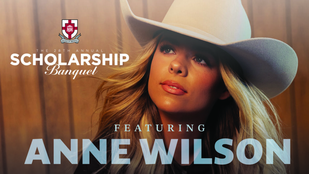 A woman in a white cowboy hat looks upward. Text reads: The 28th Annual Scholarship Banquet featuring Anne Wilson, 2026. A red and gray crest appears on the left. The background is warm brown wood.