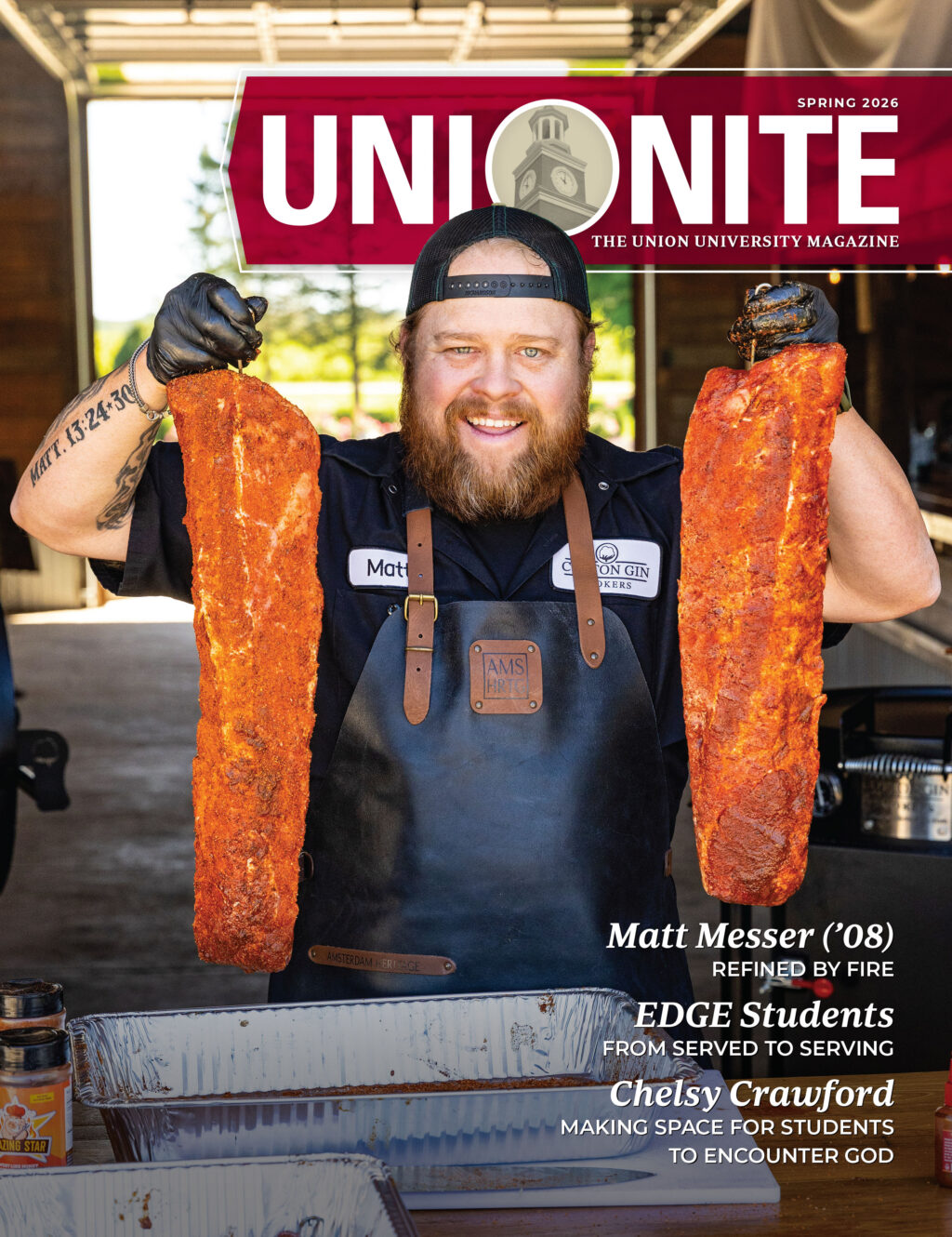 A bearded man in a black apron and gloves holds up large racks of seasoned ribs in front of him, standing inside a wooden building with open doors; magazine text overlays the image.