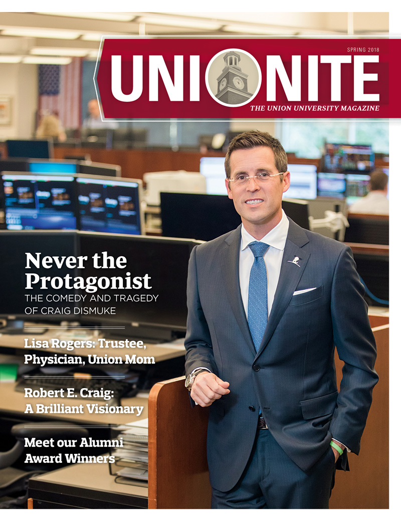 A man in a suit stands in an office with desks and computers behind him. The magazine cover reads UNIONITE and features headlines about Craig Dismuke, Lisa Rogers, Robert E. Craig, and alumni award winners.