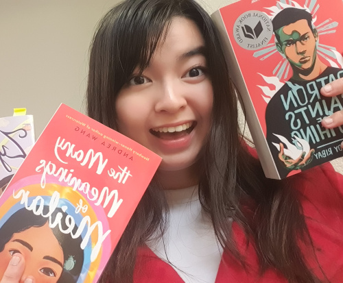 A Union senior with long dark hair is smiling and holding up two books, The Many Meanings of Meilan and Patron Saints of Nothing, in front of a beige wall, sharing publishing insights from a Penguin Random House internship.