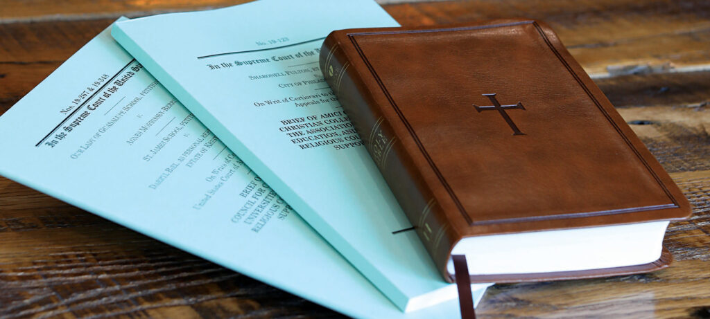 A brown leather-bound book with a cross on the cover rests on top of two light blue legal documents, symbolizing truth and unity in spirit, on a wooden surface.