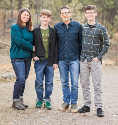 Four people stand outdoors on a dirt path with trees in the background. Casually dressed, they stand close together, smiling at the camera while celebrating the new dean of Union College's College of Arts and Sciences.