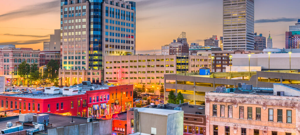 View of downtown Memphis, Tennessee at sunset, featuring tall office buildings, a multi-level parking garage, and colorful historic brick buildings in the foreground.