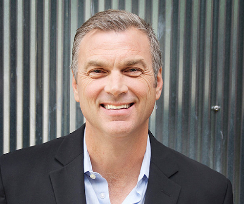 A man with short gray hair wearing a black blazer and light blue shirt smiles in front of a corrugated metal wall at a Union event on Oct. 9.