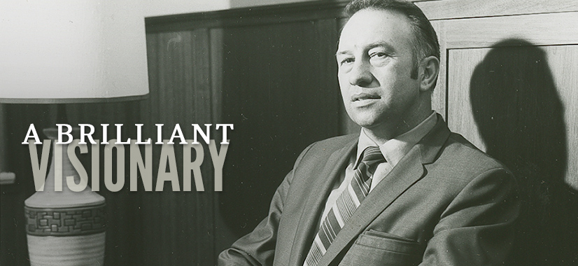 Black and white photo of a man in a suit and tie sitting beside a lamp, with the words “Brilliant Visionary” elegantly overlaid on the left side of the image.