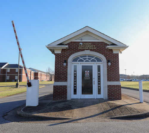 A small brick building with a peaked roof and Union University signs on the door and above the entrance. A striped security gate, part of recent safety improvements funded by a grant, is raised to the left. The building sits by a paved road with grassy areas nearby.