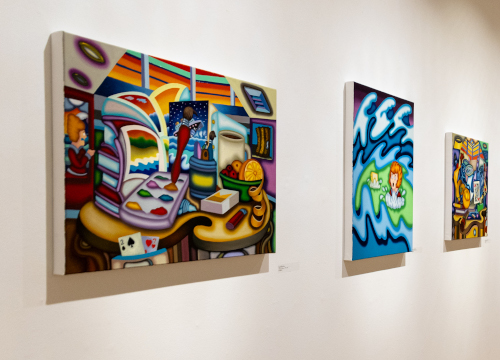 Three colorful, abstract paintings hang on a white gallery wall at the Union art gallery. The first features a busy room scene, the second depicts two people amid blue waves, and the third includes multiple figures and vivid colors.
