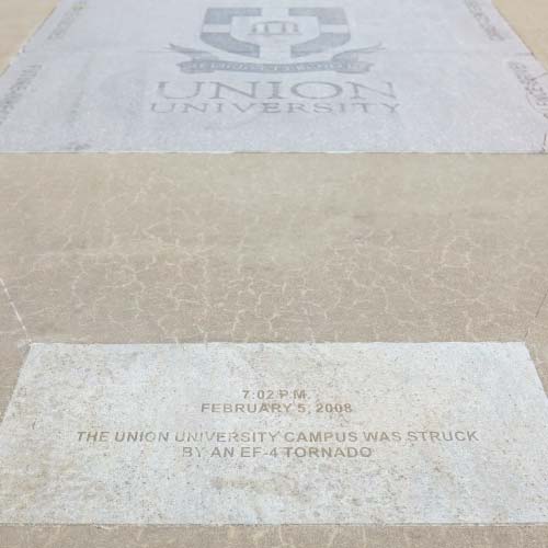 A stone marker engraved with the Union University logo and text reflects on Feb. 5, 2008, when an EF-4 tornado struck the campus at 7:02 PM. The marker is set in a concrete walkway for reflection and remembrance.