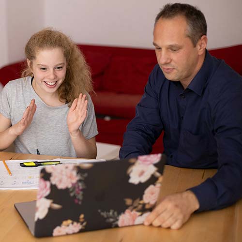 A man and a young girl sit at a table, looking at a laptop with a floral case. The girl is smiling with raised hands, excited to learn ACT tips, while the man is focused on the screen. Papers, a pen, and a highlighter are on the table.