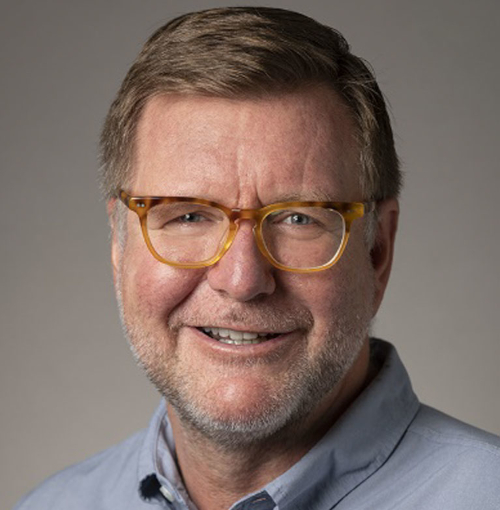 A middle-aged man with short light brown hair, wearing tortoiseshell eyeglasses and a light blue collared shirt, smiles at the camera against a plain background, reminiscent of speakers at the Carls-Schwerdfeger History Lectures on Oct. 14.