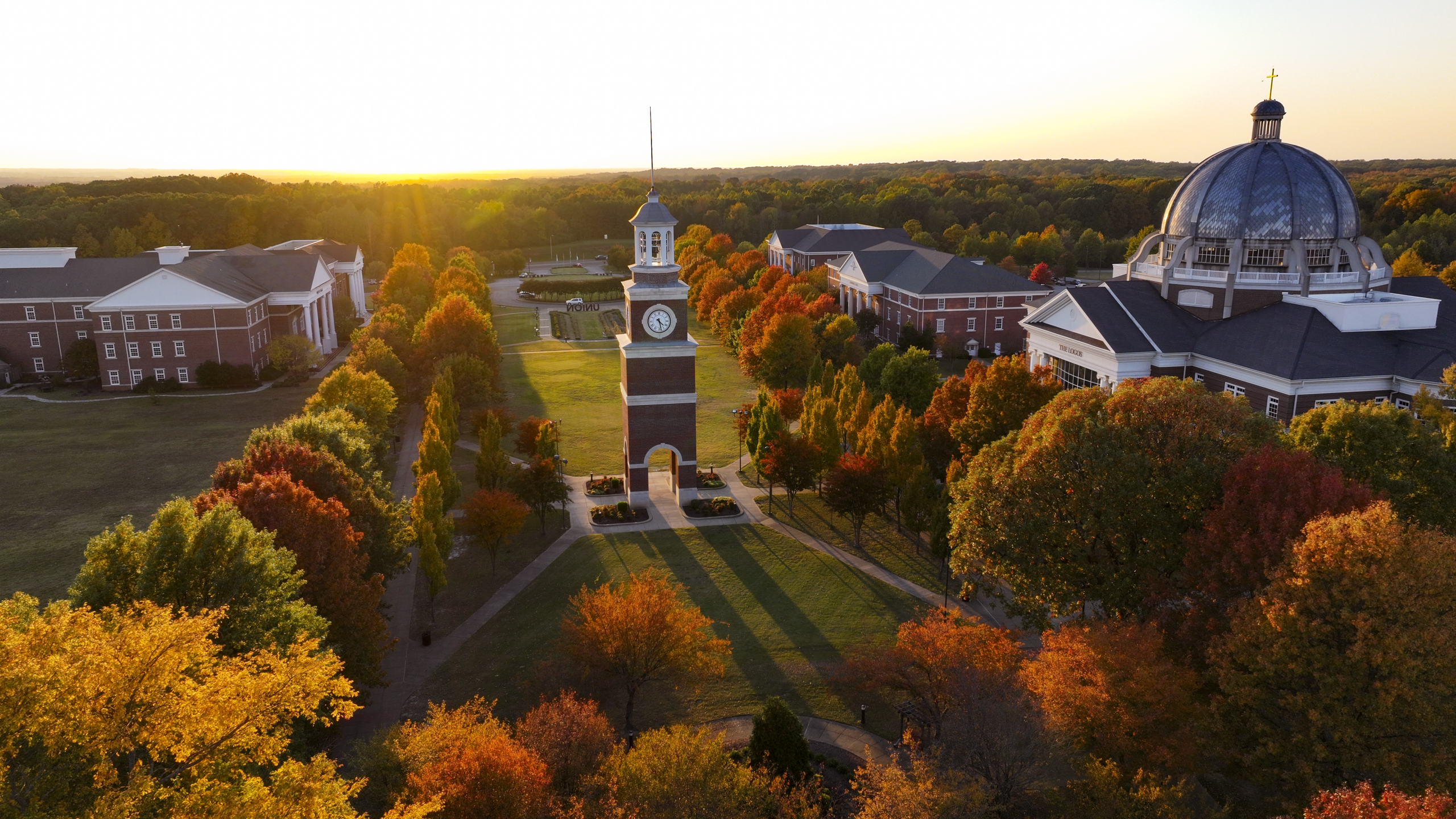 Aerial view of Union's main campus in Jackson, Tennessee, at sunset, featuring a central clock tower, red-brick buildings, a domed structure, and trees with autumn foliage.