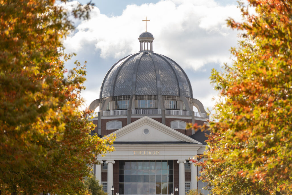 A domed building with a cross on top, framed by trees with autumn leaves. Located in Tennessee, Union's main campus is in Jackson. The building features columns, large windows, and the words THE LOGOS above the entrance.