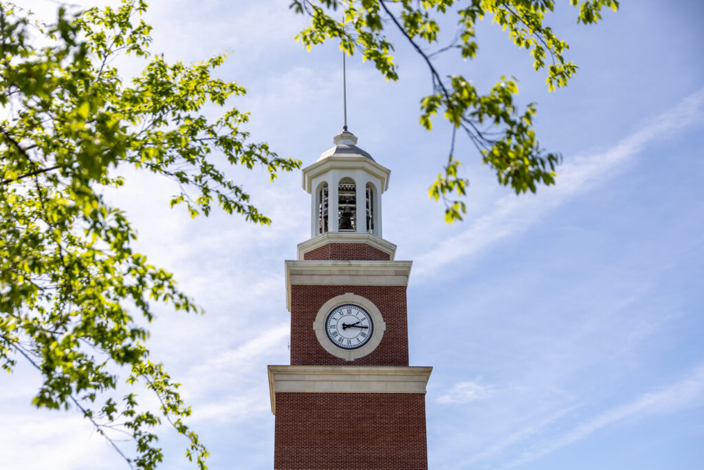 A red brick clock tower with a white clock face and cupola, surrounded by green tree branches, stands against a clear blue sky on Union's main campus in Jackson, Tennessee.
