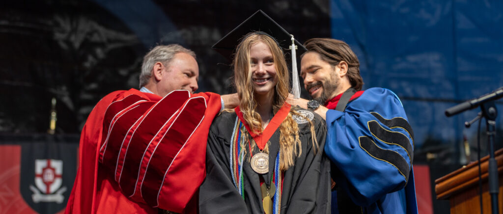 A young graduate smiles on stage as two faculty members in academic robes place a medal around her neck during Union commencement, celebrating the special moments of graduation 2024.