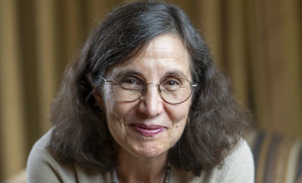 A woman with shoulder-length brown hair, glasses, and a beige top is smiling gently at the camera. The softly blurred background in brown and gold tones evokes the warmth of the Crabtree Family Life Series.