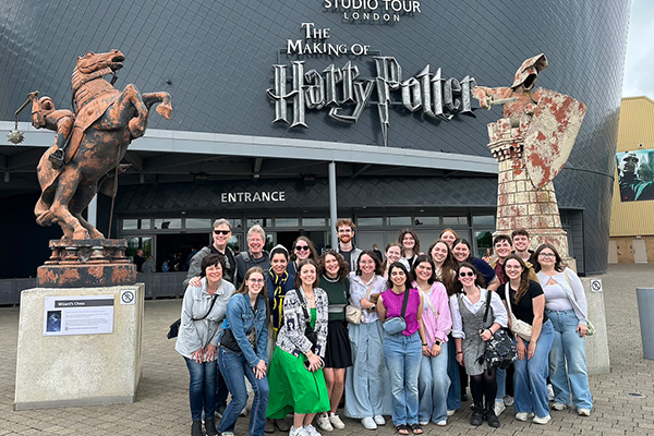 A group of people pose in front of the entrance to The Making of Harry Potter Studio Tour in London, UK, flanked by large stone statues and a wall displaying the tour name.