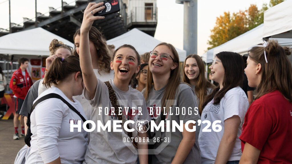 A group of young people laughing while taking a selfie at a Forever Bulldogs Homecoming 2026 event, with October 26-31 overlaid on the image.